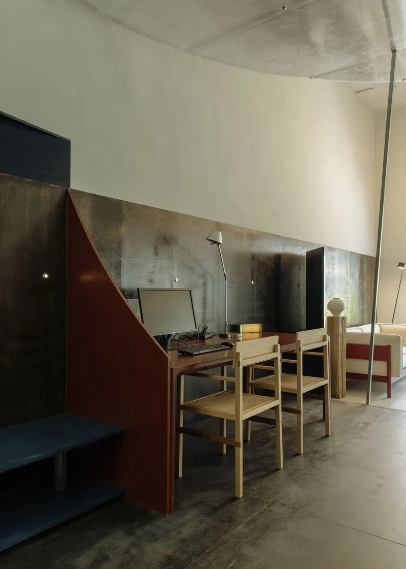 Dining area with timber chairs and maroon partition wall set against variegated metal panel backdrop