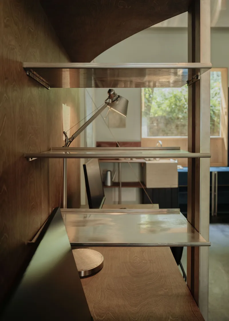 Built-in shelving unit with articulated desk lamp and sliding work surfaces in timber and metal