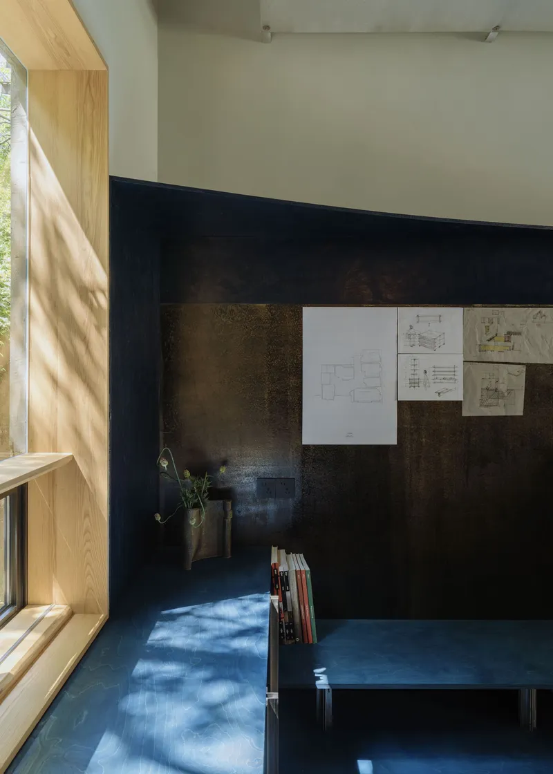 Dark steel wall with blue bench and scattered daylight from adjacent timber-framed window