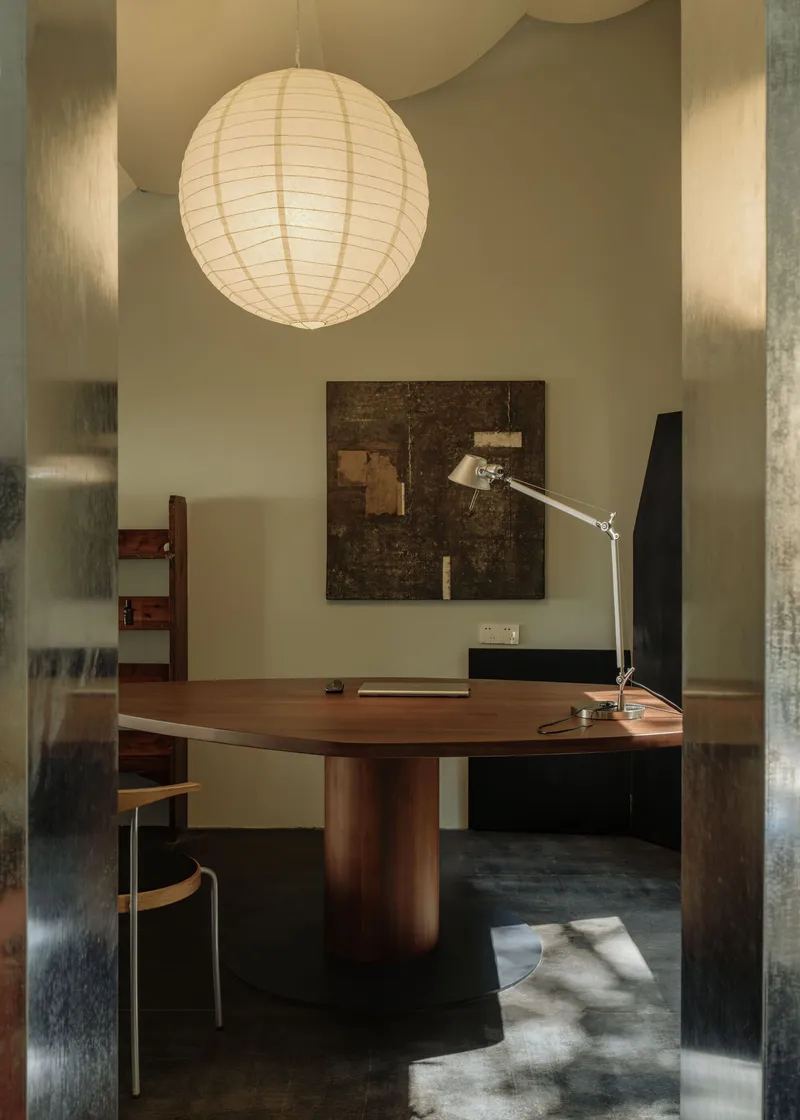 Office with circular walnut table beneath a paper lantern and sunlight falling across dark flooring