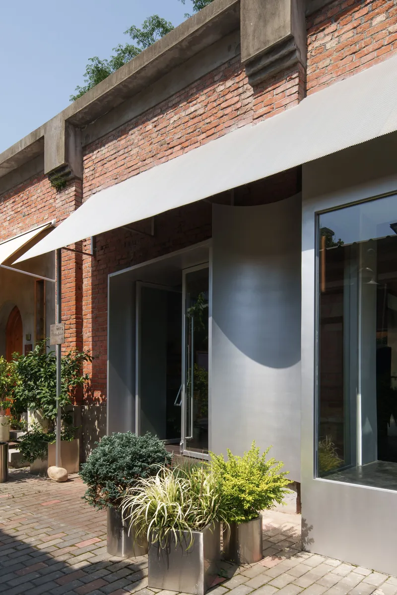 Exterior facade with exposed brick upper band and white render below planted containers