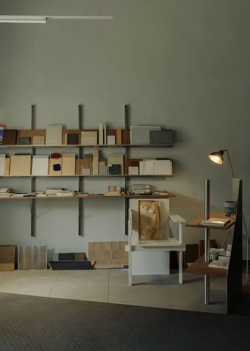 Wall-mounted shelving system holding architectural models and material samples with desk lamp