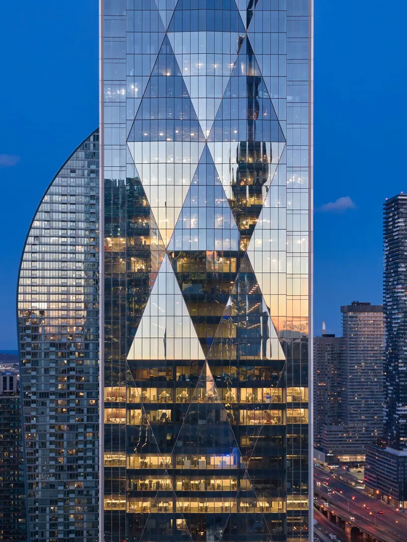 Close-up of glass facade with triangular structural bracing reflecting adjacent buildings at blue hour