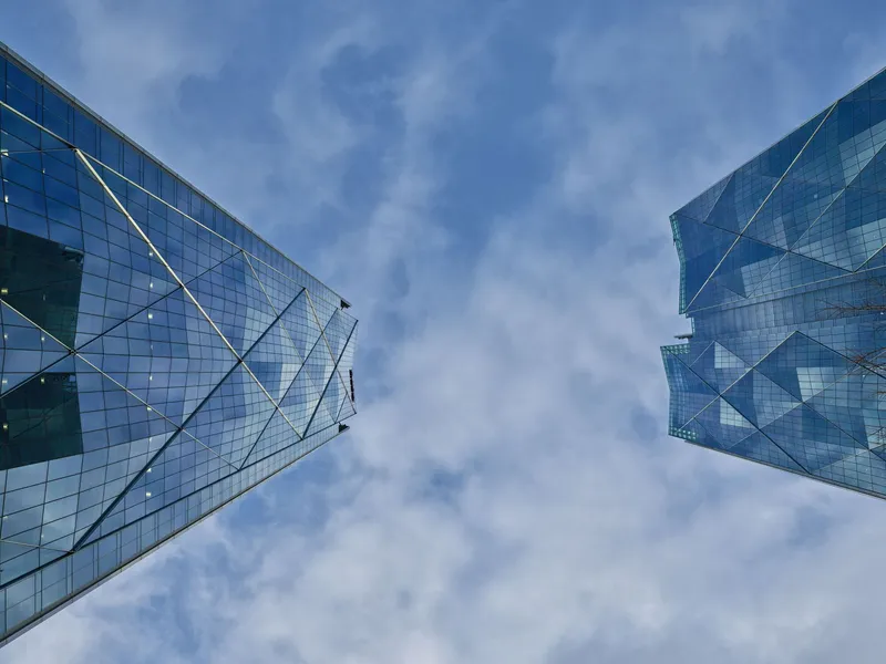 Upward view of the diagonal bracing on the glass curtain wall against a partly cloudy sky