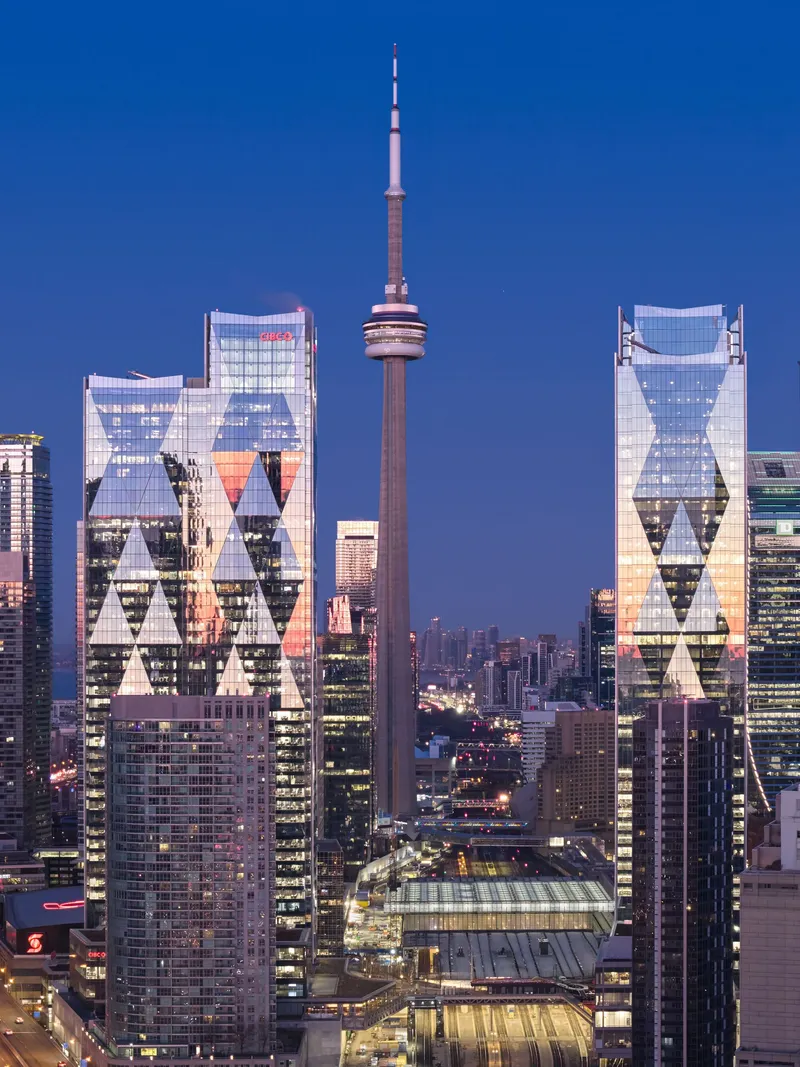 Twin glass towers with triangular window patterns illuminated against the deep blue evening sky