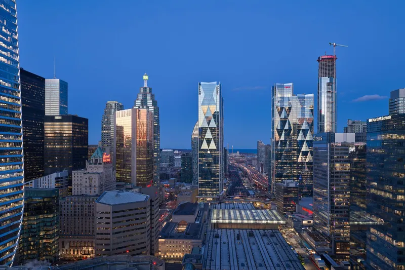 Skyline perspective with the paired towers and adjacent glass-roofed transit station at twilight