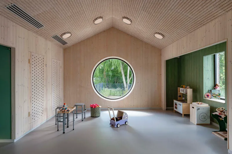 Playroom with pale timber walls, ribbed ceiling and circular window framing birch trees outside