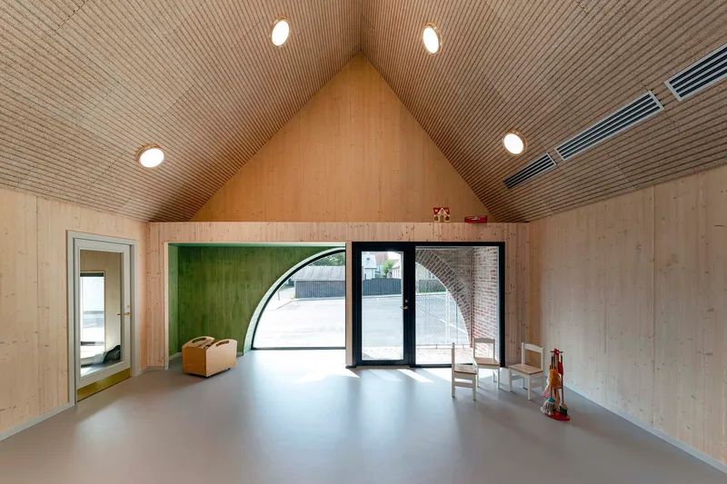 Open room with pale timber walls, gabled ribbed ceiling and arched glazed door to courtyard
