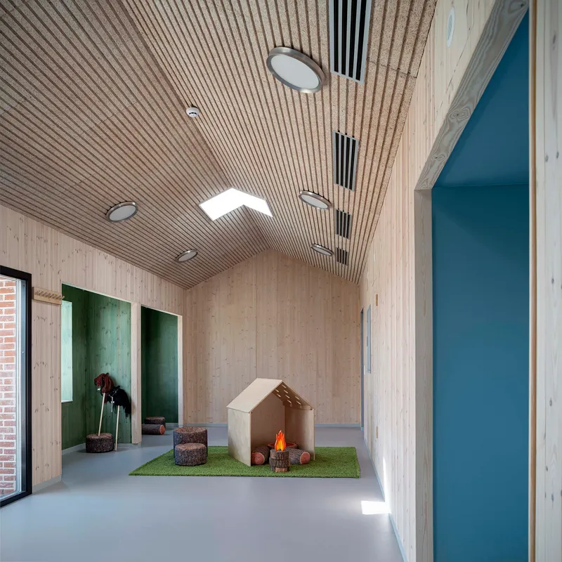 Corridor with ribbed timber ceiling, skylights and plywood play structure on artificial grass mat