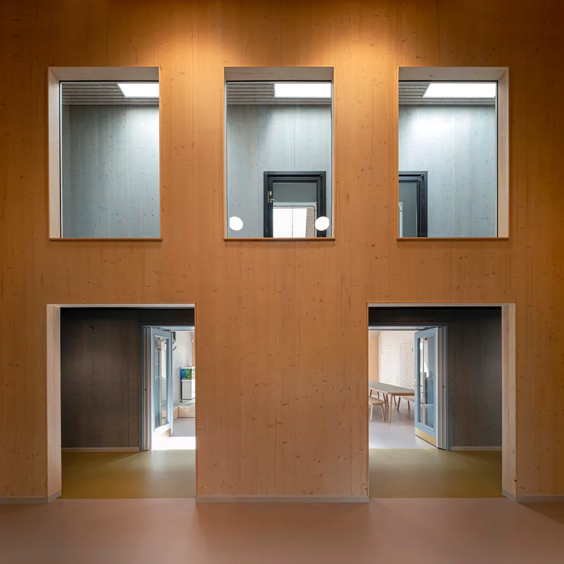 Plywood wall with three recessed windows above and two doorways opening to interior spaces