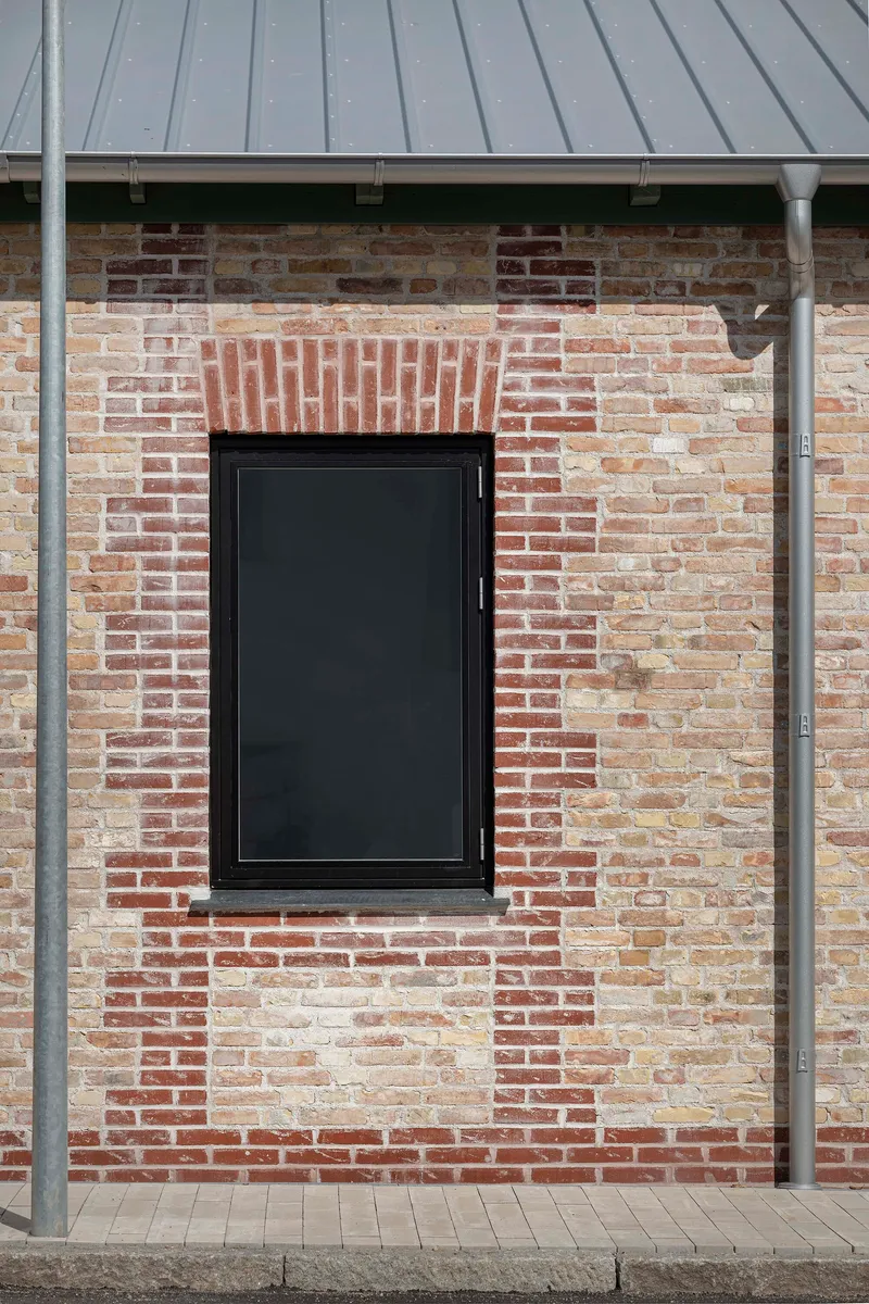 Black-framed window set in reclaimed brick wall with decorative brickwork header beneath a metal overhang
