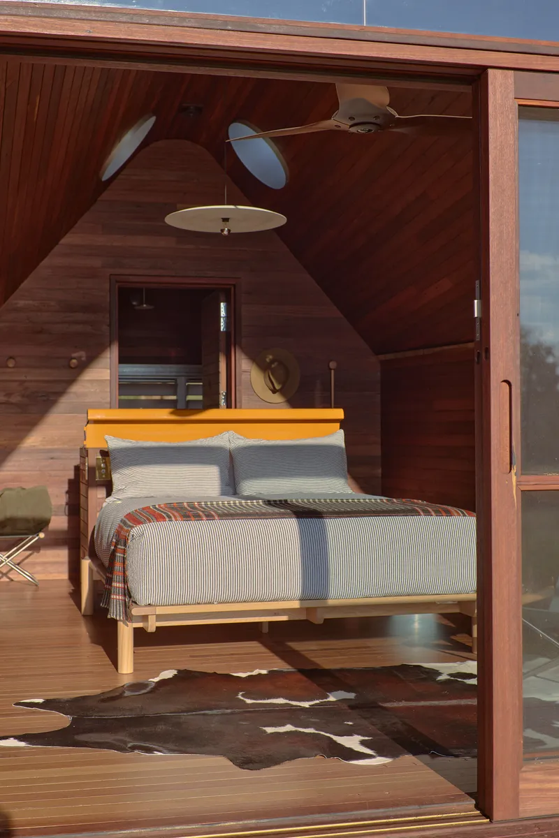 Bedroom with timber flooring and walls framed by sliding glass doors in afternoon sunlight