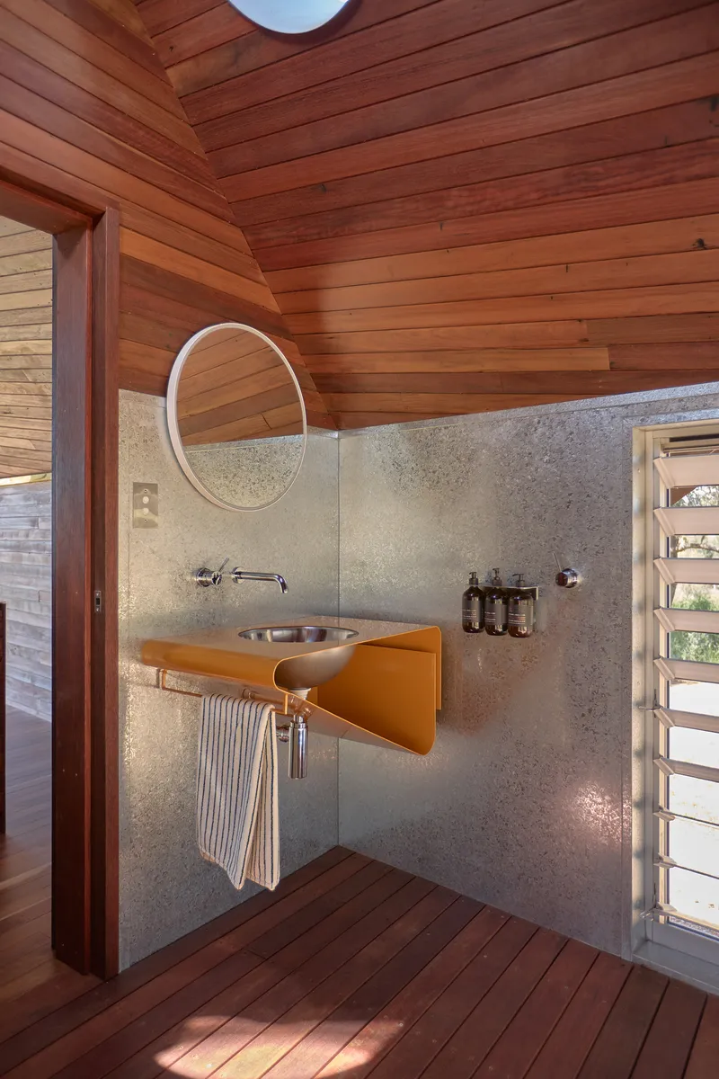 Corner bathroom with wall-mounted basin on yellow console and textured concrete backsplash under wood ceiling