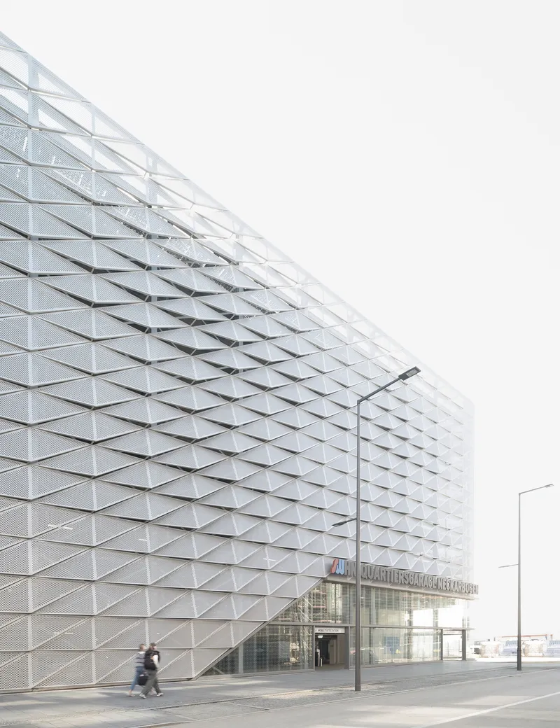 Triangulated metal facade with embedded glass panels at street level with a person walking past