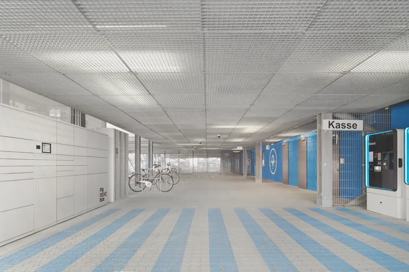Interior ground level entry hall with metal mesh ceiling and striped pavers leading to bicycle parking