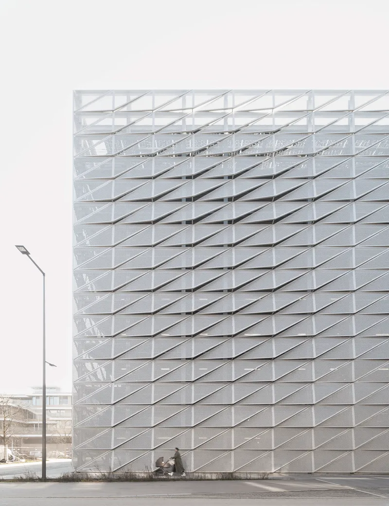 White folded panel facade with diagonal grid pattern and pedestrians at ground level under overcast sky