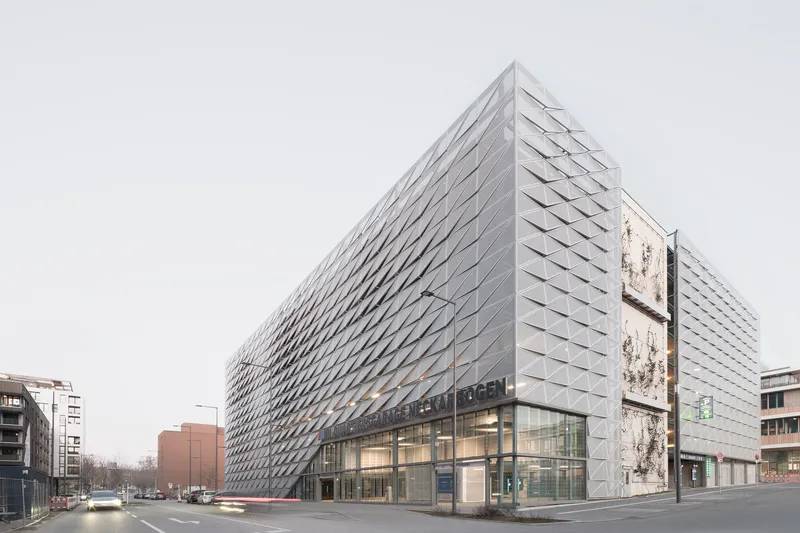 Street view showing the glass-walled base beneath the geometric metal-clad volume at dusk