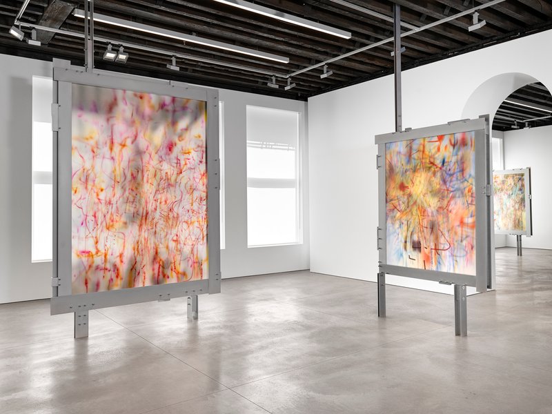Gallery room with freestanding gray steel frames holding artwork under exposed timber joists
