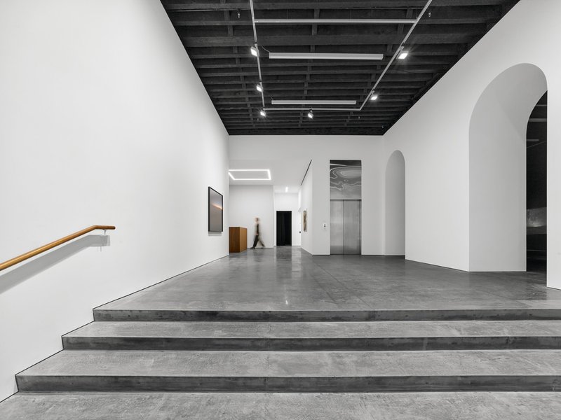 Wide concrete stairs with timber handrail leading to gallery space with arched doorways