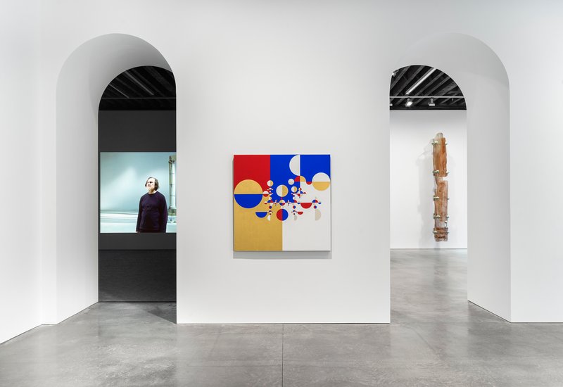 White gallery wall with paired arched openings and concrete floor displaying artwork between them