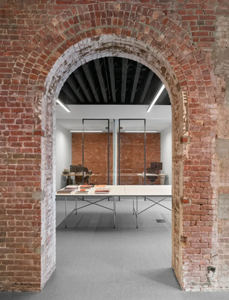 View through exposed brick archway into gallery space with display table and suspended brick panels