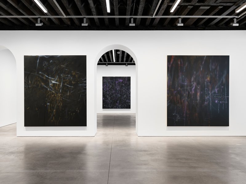 White exhibition wall with arched opening framing view through to adjacent gallery room
