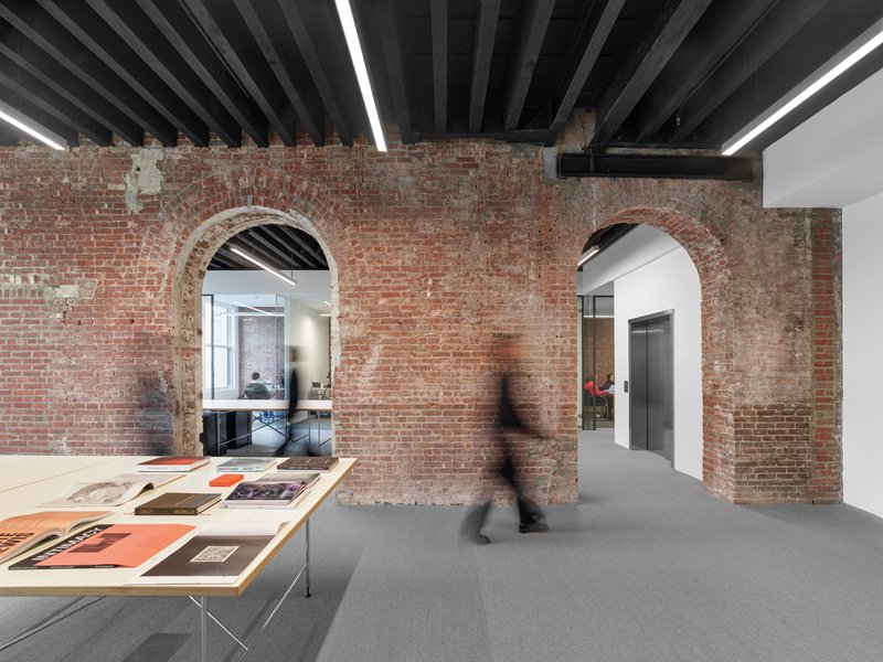 Exposed brick wall with arched openings beneath black painted timber joists and linear lighting