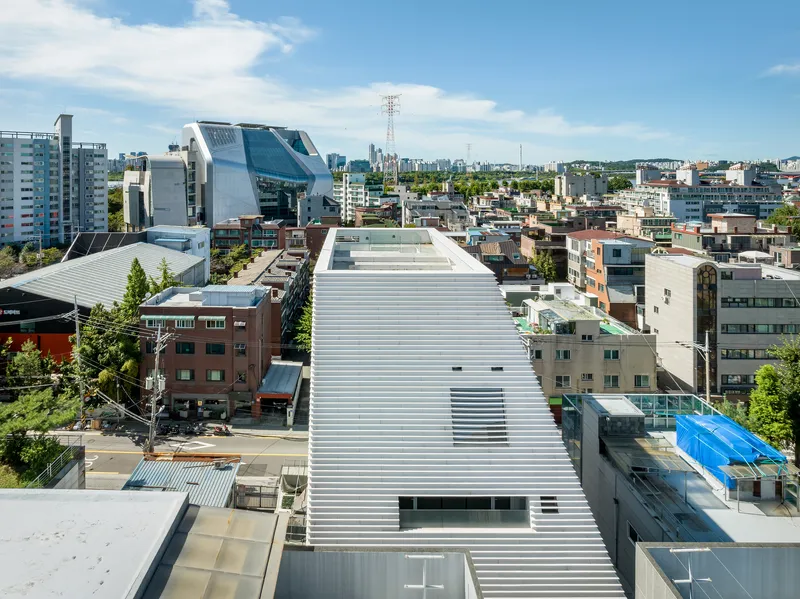 Elevated view of the horizontal louver roof extending across the dense neighborhood under summer sky