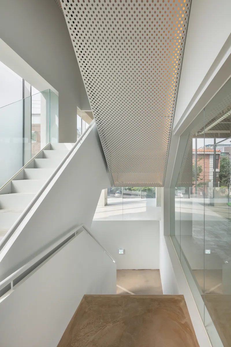 Stair landing with angled perforated metal ceiling and glass walls overlooking adjacent spaces