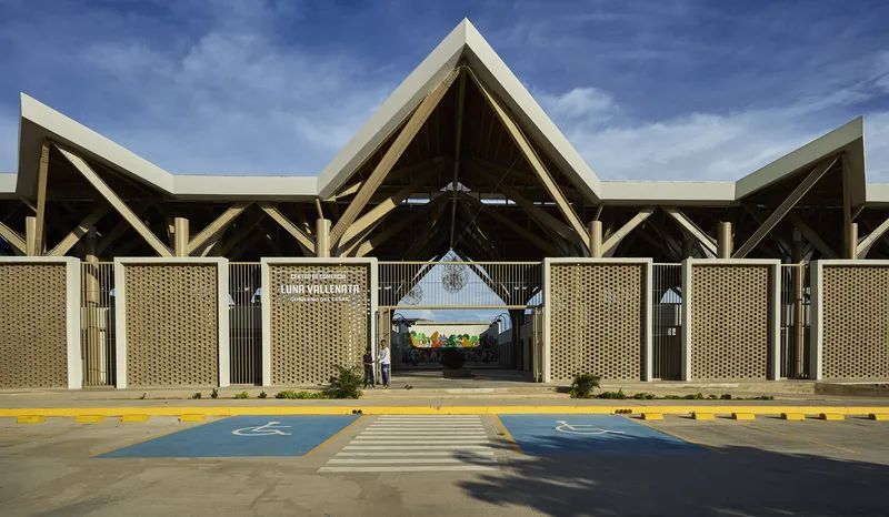 Entry facade with woven lattice panels between white piers and triangular gabled roof forms under blue sky