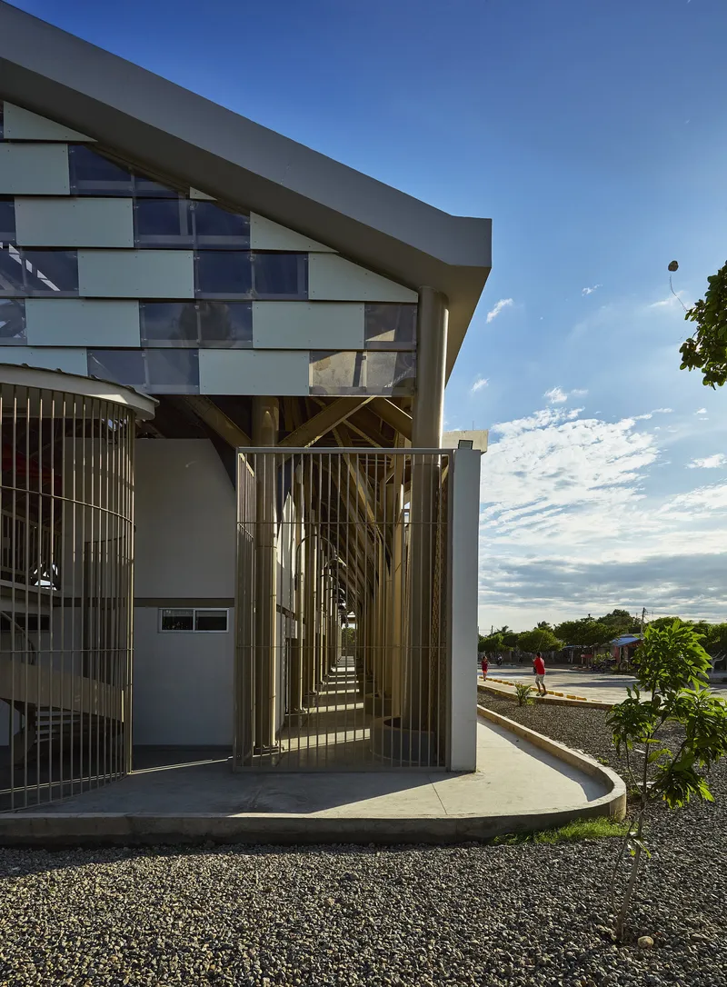 Entrance with vertical metal screen and curved concrete platform under a cloudy afternoon sky