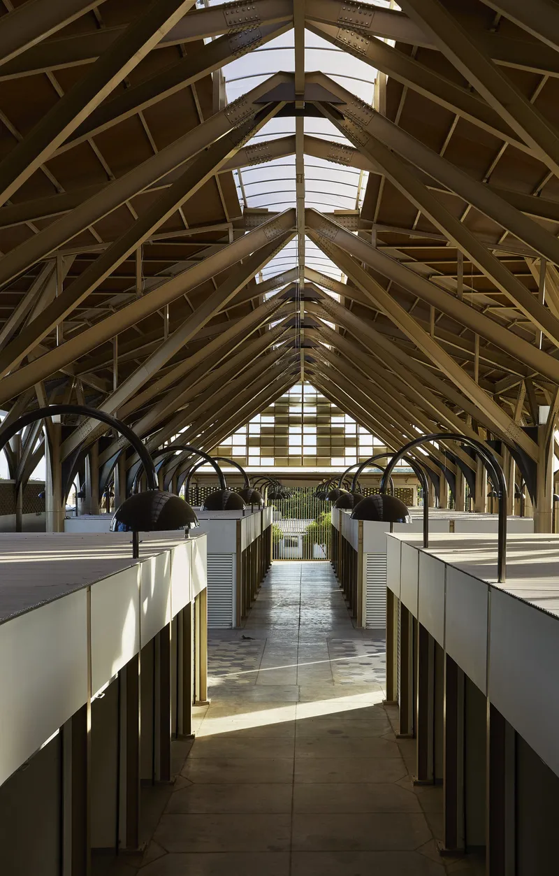 Central aisle with timber arched ceiling, skylights, arched pendant lamps, and flanking vendor stalls