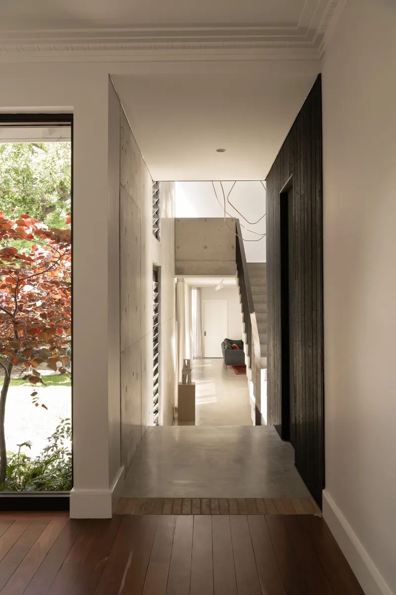 Hallway with concrete floor and charred timber walls looking through to a courtyard window framing red foliage