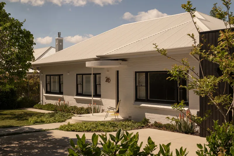 Front facade with corrugated metal roof and planted garden beds under afternoon light