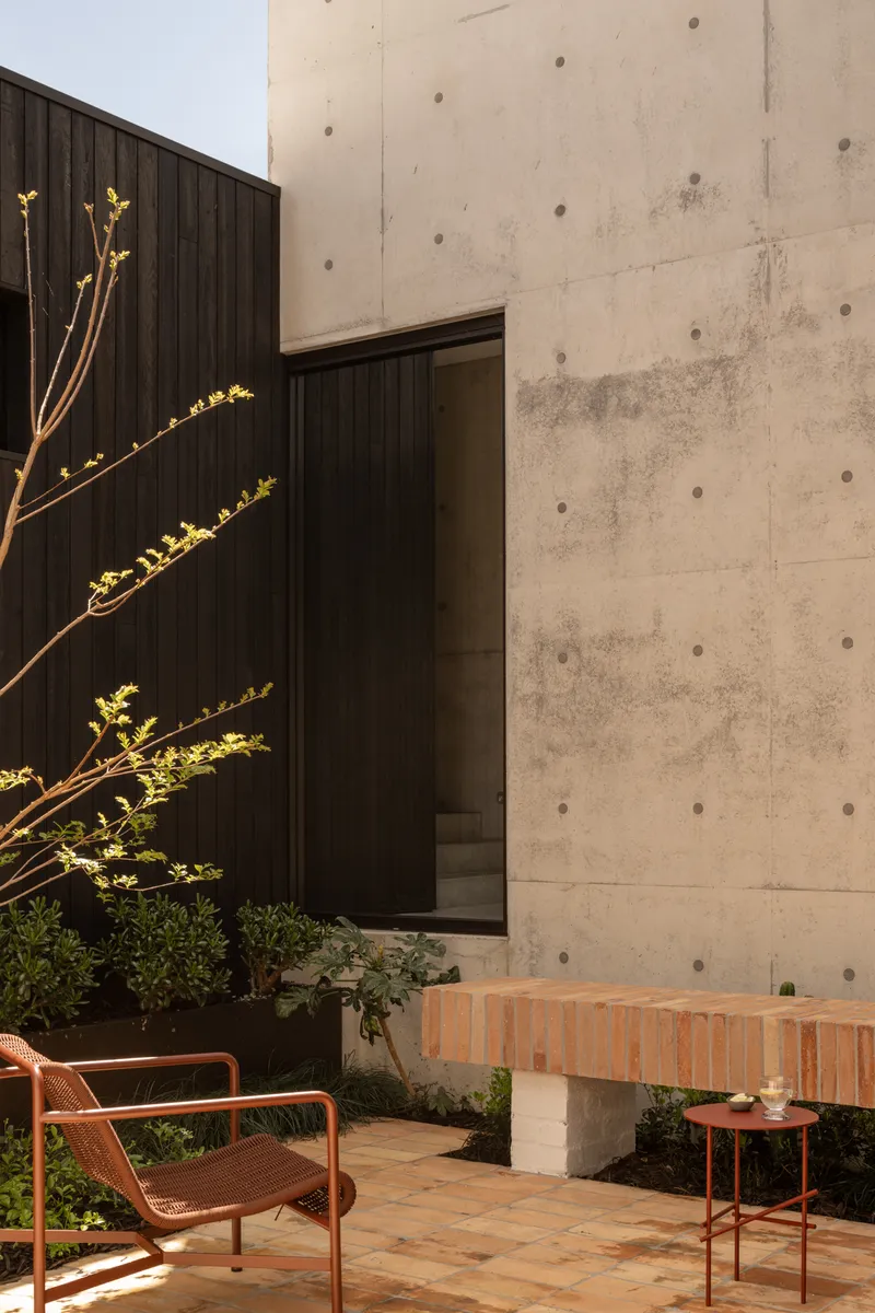 Board-formed concrete wall meeting timber cladding with doorway and terracotta brick bench