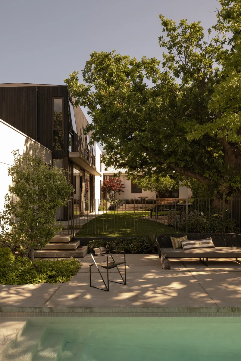 Courtyard pool terrace with dappled sunlight beneath a mature tree canopy at dusk
