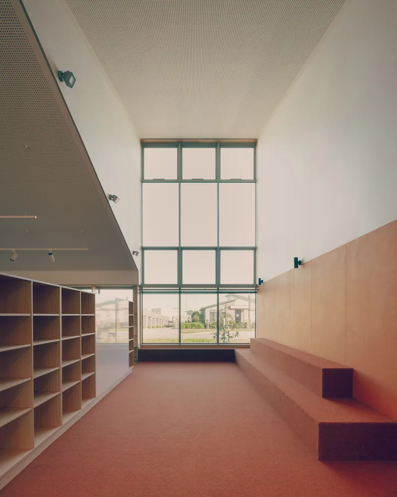 Reading nook with two-story gridded window overlooking the campus and built-in plywood seating along the wall