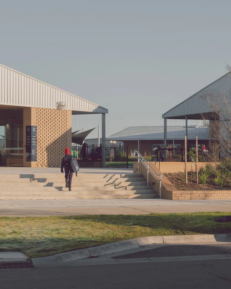 Timber steps and perforated brick retention wall leading between two pavilions with corrugated metal cladding