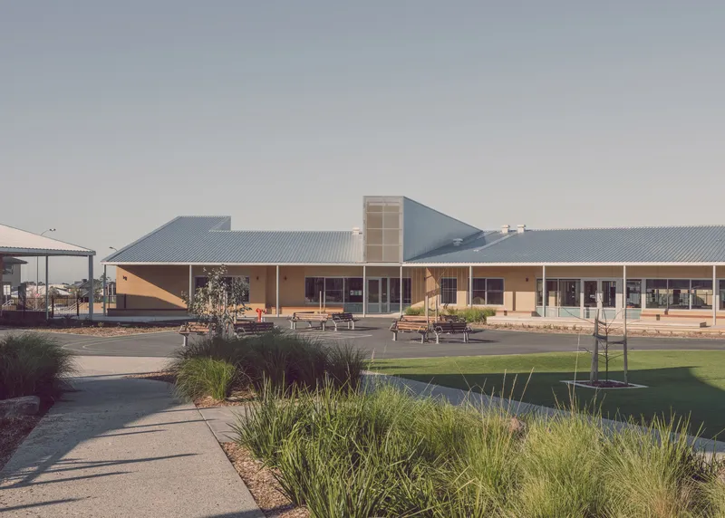 View across landscaped courtyard with native grasses toward the low-slung corrugated metal roofed school complex