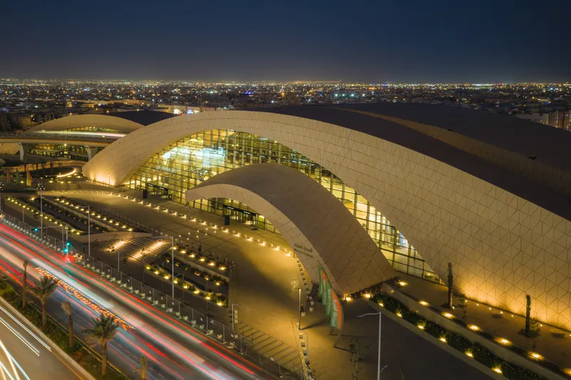 Aerial night view of the curved roof with illuminated glass facade and surrounding traffic streaks