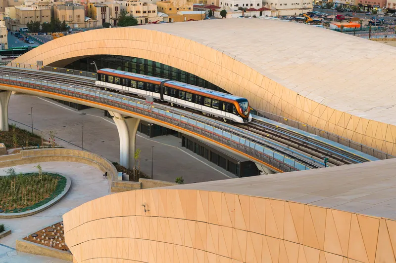 Train emerging from beneath the curved tiled canopy supported by concrete columns at golden hour