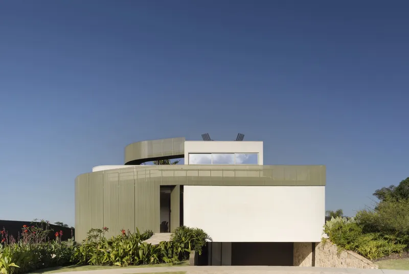 Street facade combining vertical metal cladding and white plaster volumes under a clear blue sky