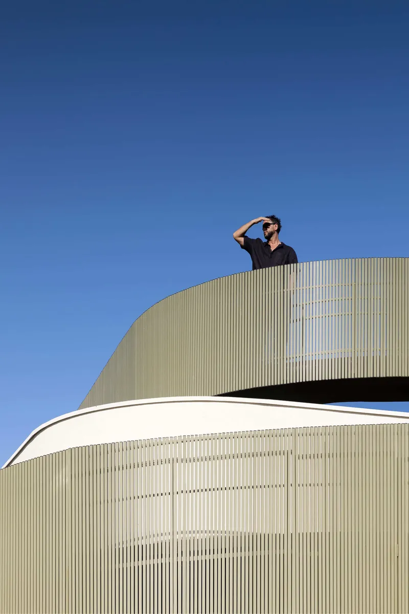 Curved roof terrace clad in vertical metal fins with a person standing against blue sky