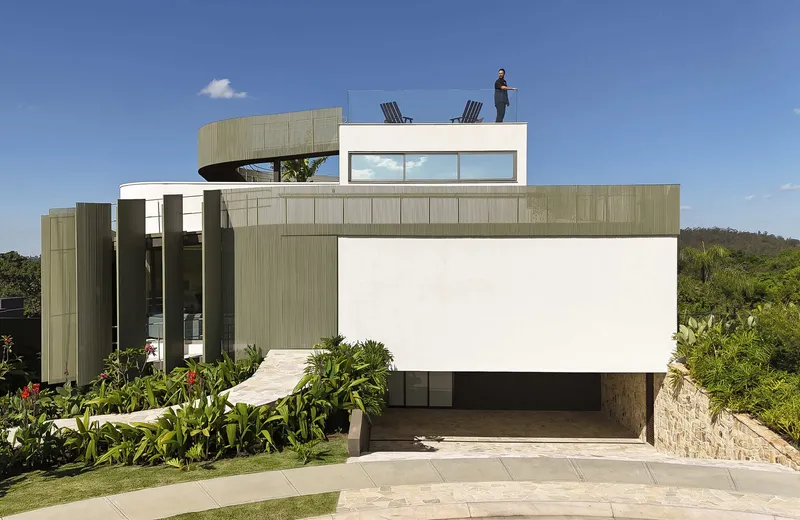 Street view of the residence with vertical timber cladding, recessed carport and a figure on the roof terrace