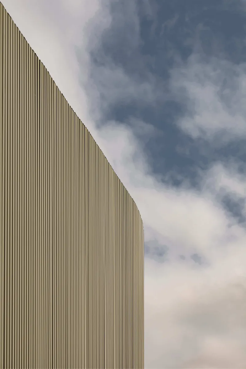 Angled corner of the vertically ribbed timber facade against a cloudy sky