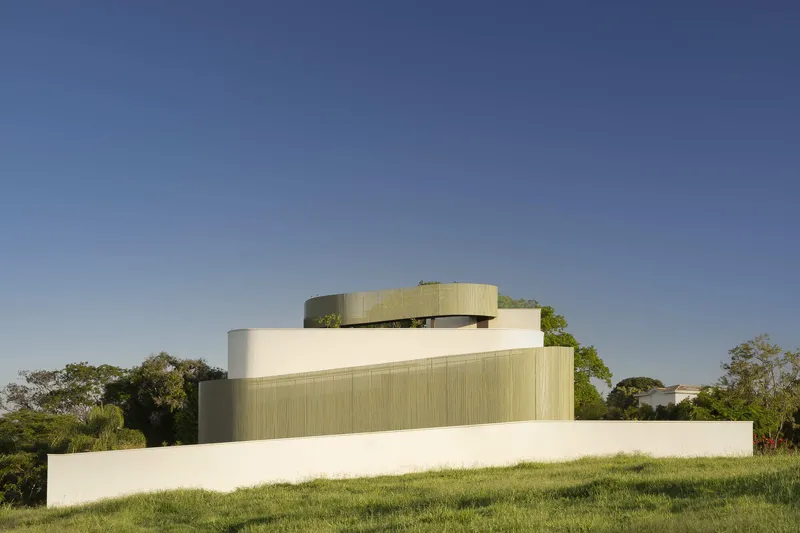 Rear elevation showing stacked volumes with curved and ribbed cladding rising from a grassy slope