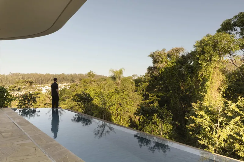 Infinity pool overlooking dense forest canopy with a figure standing at the edge