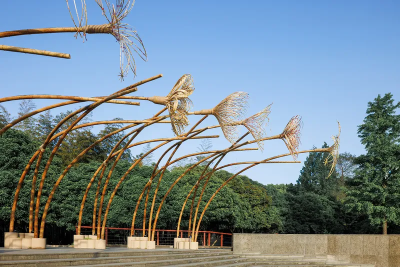 Curved bamboo arches with woven bird sculptures anchored to concrete footings under a clear blue sky