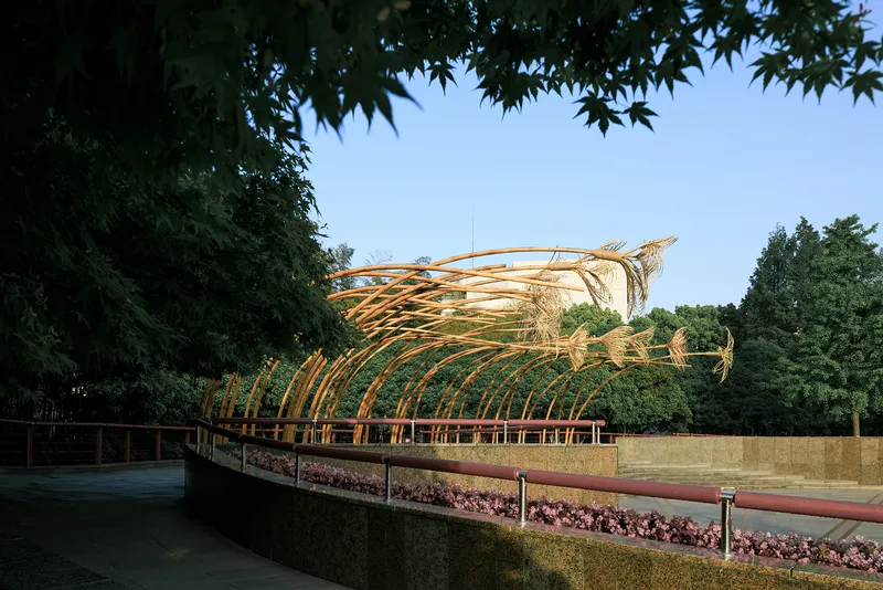 Arching bamboo canopy over a planted terrace framed by overhanging maple branches at dusk