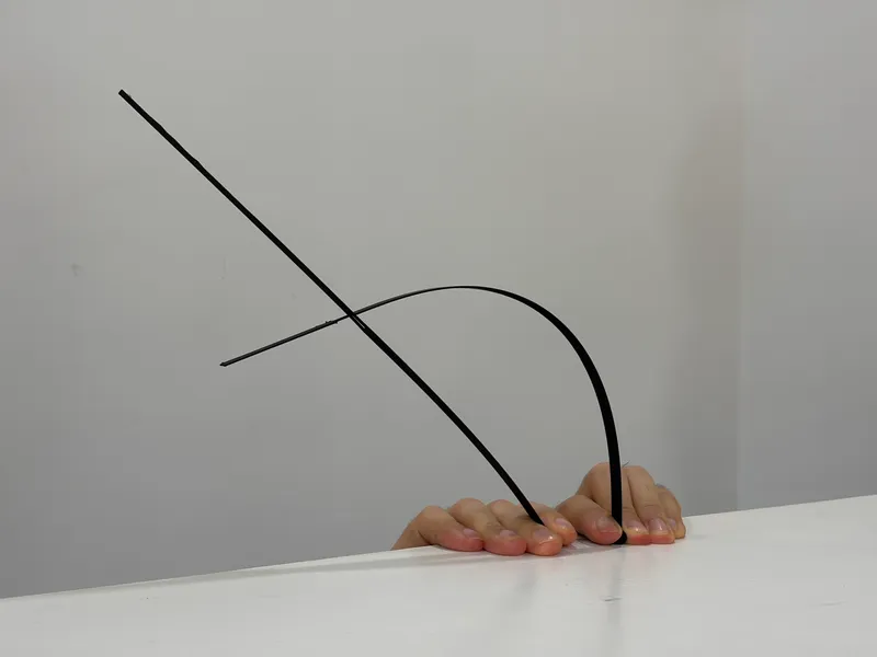 Close-up of a hand emerging from beneath a white surface holding bent metal rods